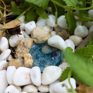 May include: A blue resin paperweight with glitter embedded in the resin. The paperweight is surrounded by white and brown stones.