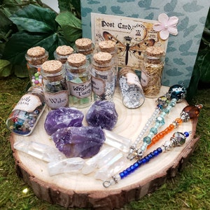 May include: A collection of small glass bottles with cork tops filled with various colorful items, including beads, glitter, and crystals. The bottles are arranged on a wooden slice with amethyst crystals and three beaded wands.