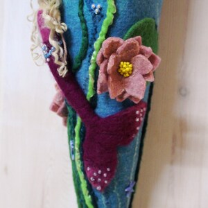 May include: A felt mermaid tail ornament with a pink flower, green seaweed, and a blue seahorse. The mermaid has long blonde hair and a pink tail.
