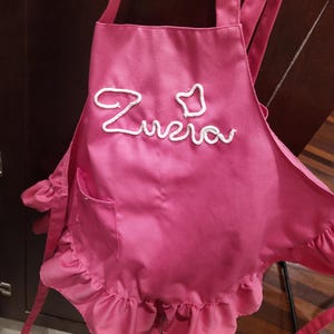 May include: A pink ruffled apron with white embroidery that says "Zuzia".