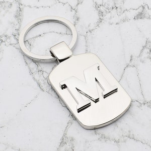 Llavero de plata personalizado con diseño de letra inicial y grabado en la parte posterior.