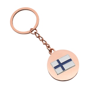 May include: A rose gold keychain with a circular charm featuring the Finnish flag. The flag is white with a blue cross.