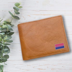 May include: A brown leather wallet with a small bisexual pride flag pin on the lower right corner.