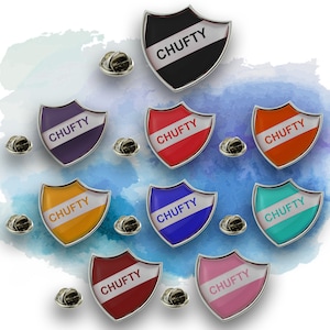 May include: Ten colorful enamel pins in the shape of a shield with the word "CHUFTY" written on each pin. The pins are arranged in a circle on a blue watercolor background.