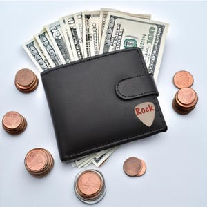 May include: A black leather wallet with a guitar pick that says "Rock" on it. The wallet is open and filled with US dollar bills. There are stacks of copper coins scattered around the wallet.