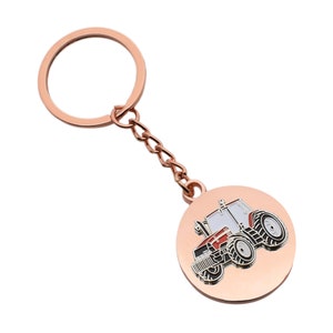 Può includere: Un portachiavi in metallo color oro rosa con un ciondolo rotondo che raffigura un trattore rosso e nero con dettagli bianchi.
