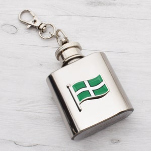 May include: A silver flask with a green and white flag design. The flask has a silver cap and a silver chain with a clip.