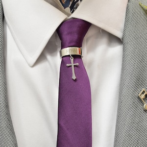 Puede incluir: Una corbata morada con un clip de corbata plateado con una cruz y la inscripción "SDW".