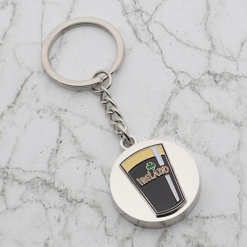 May include: Silver keychain with a round metal charm featuring a black and gold pint glass with the word "IRELAND" and a shamrock.