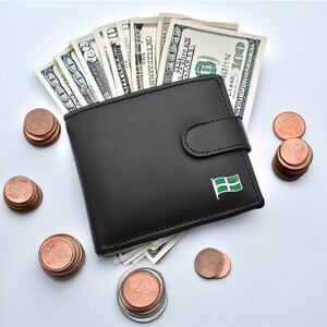 May include: A black leather wallet with a green and white flag pin. The wallet is open and filled with US dollar bills. There are stacks of copper coins scattered around the wallet.