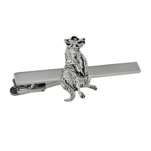 May include: Silver tie bar featuring a meerkat figurine. The bar is engraved with the word "MEH".