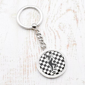 May include: Silver keychain with a round, black and white checkered charm featuring a silhouette of a person in a suit dancing.