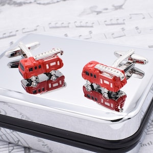 May include: A pair of silver cufflinks with red fire truck designs. The trucks have ladders and are detailed with black accents.