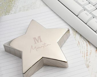 May include: A silver star-shaped desk accessory with the letter "M" and the name "Martin" engraved on the top. The star is on lined paper next to a white keyboard.