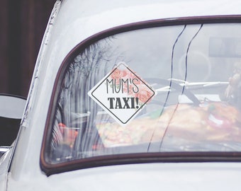 Puede incluir: Coche blanco con un letrero en forma de diamante rosa y blanco con flores que dice "MUM'S TAXI!" en la ventana trasera.