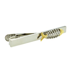 Könnte beinhalten: Silberne Krawattennadel mit einem goldenen Fischdesign. Der Fisch ist aus Metall und hat ein detailliertes Design.