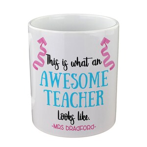 May include: White ceramic mug with pink and blue text that reads "This is what an AWESOME TEACHER looks like. -MRS BRADFORD-."  The text is surrounded by pink swirls.
