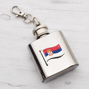 Op de afbeelding: Een zilveren fles met een sleutelhanger eraan. De fles heeft een kleine, kleurrijke vlag van Servië aan de voorkant.