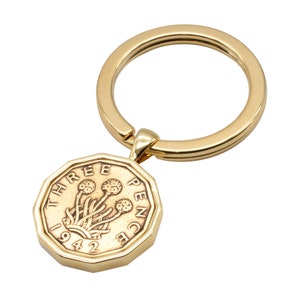 May include: Gold-colored key chain with a three pence coin from 1942 attached. The coin features a design of three thistles.