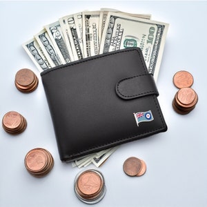 May include: A black leather wallet with a small flag pin on the front. The wallet is open and filled with US dollar bills. There are stacks of copper coins scattered around the wallet.