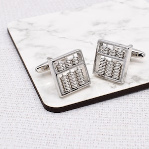 May include: A pair of silver abacus cufflinks. The cufflinks are square shaped and feature a silver abacus with beads.