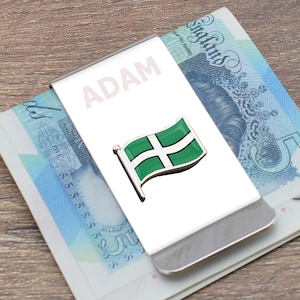 Può includere: Un fermaglio per soldi in argento con il nome "ADAM" stampato su di esso. Una bandiera verde e bianca con una croce bianca è attaccata al fermaglio.