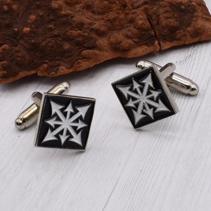 May include: A pair of silver cufflinks with a black and white enamel design. The design features a stylized star with eight points and arrows pointing outward from each point.