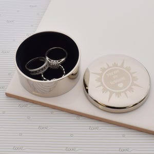 May include: Silver round trinket box with a blue velvet interior. The lid has a sun design with the text "You are my sunshine" and a heart.