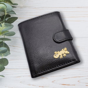 May include: Black leather wallet with a gold-colored lizard emblem. The wallet has a textured surface and a snap closure. The lizard emblem is a decorative accent on the front of the wallet.