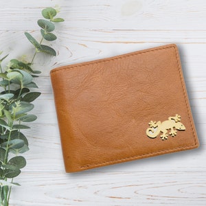 Könnte beinhalten: Eine braune Ledergeldbörse mit einem goldenen Eidechsen-Design auf der Vorderseite.
