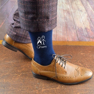 May include: A pair of navy blue socks with a white design of a bride and groom. The socks have the word "Groom" written on them.