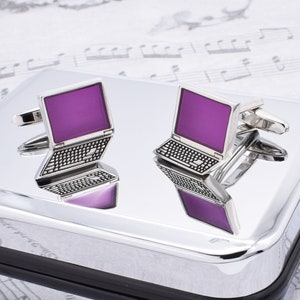 Puede incluir: Un par de gemelos de plata con forma de portátil con pantallas moradas. Los gemelos están sobre un fondo plateado.