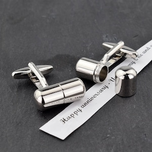 May include: Silver cufflinks with a small, cylindrical compartment that opens. The cufflinks are on a white card with the text "Happy anniversary -  You and my One and only".