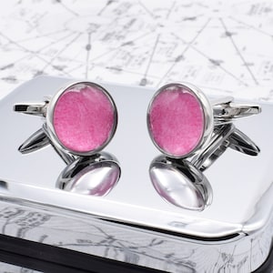 May include: A pair of silver cufflinks with pink resin inserts. The cufflinks are round and have a smooth, polished finish.