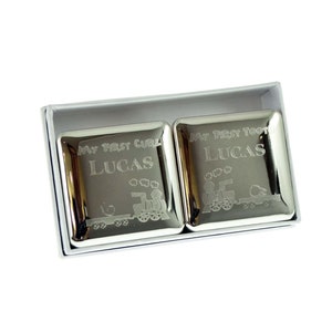 Könnte beinhalten: Zwei silberne Erinnerungsboxen mit gravierten Zugmotiven. Die Boxen sind mit "My First Curl Lucas" und "My First Tooth Lucas" beschriftet.