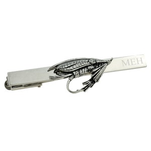 Könnte beinhalten: Silberne Krawattenklammer mit einem detaillierten Design einer Fliegenfisch-Köder und dem Wort "MEH" auf der Klammer graviert.