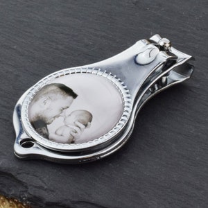 May include: Silver nail clippers with a round photo insert featuring a black and white photo of a father and baby.