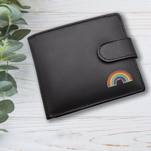 May include: A black leather wallet with a rainbow-coloured enamel pin of a rainbow arch. The wallet has a flap closure with a button.