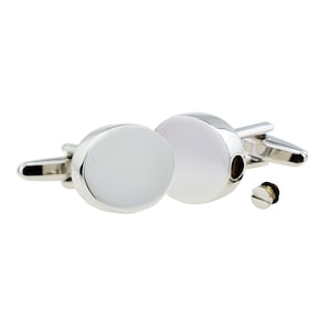 May include: A pair of silver oval cufflinks with a smooth, white surface. One cufflink has a small, round opening on the side.