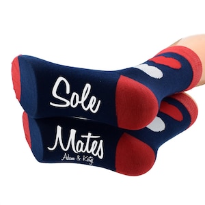 Op de afbeelding: Een paar blauwe en rode sokken met witte stippen. De sokken hebben de tekst "Sole Mates" erop staan, met de namen "Adam & Katy" eronder.