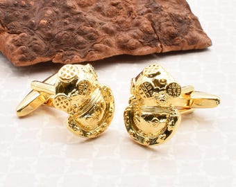 May include: A pair of gold-tone cufflinks featuring a detailed design of a vintage diving helmet.