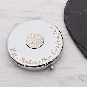 Puede incluir: Un espejo compacto plateado con una pequeña moneda en su interior. El espejo está grabado con el texto "Happy Birthday Mum Love Jennifer x".