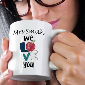 May include: White ceramic mug with a black handle. The mug has a design that says "Mrs. Smith we love you" with a red apple and colourful pencils and paper.