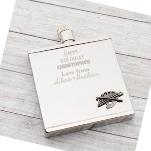 May include: A silver flask with a textured cap. The flask is engraved with "Happy Birthday Christopher, Love from Silvie & Graham." A small metal artist's palette and brushes are on the lower right.