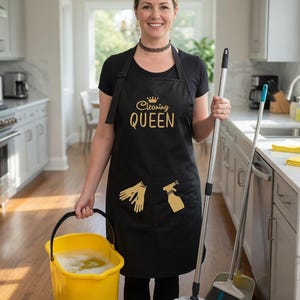 以下が含まれることがあります： 金色の「Cleaning QUEEN」の文字と、金色の手袋とスプレーボトルのグラフィックが入った黒いエプロン。黄色いバケツとモップを持っています。ほうきとちりとりも写っています。
