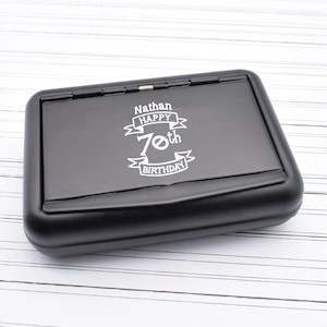 Könnte beinhalten: Schwarze Metall-Geschenkbox mit einer personalisierten Inschrift, die "Nathan Happy 70th Birthday" lautet.