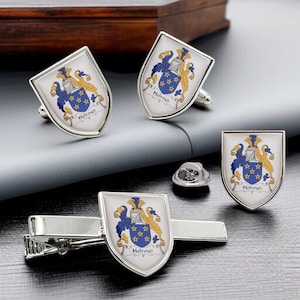 Puede incluir: Un conjunto de accesorios plateados con un diseño de escudo familiar. El conjunto incluye gemelos, un clip para corbata, un pin de solapa y un emblema en forma de escudo con detalles azules, dorados y blancos. El nombre de la familia "Holroyd" está impreso.