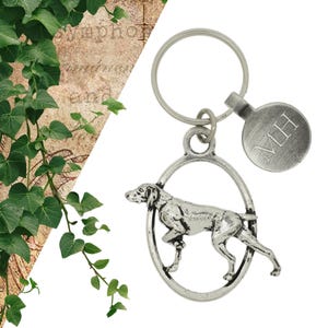 May include: Silver-toned keyring featuring a detailed German Shorthaired Pointer dog silhouette. The dog is standing in a circular frame. The keyring also includes a round tag with the initials "MH" engraved on it.