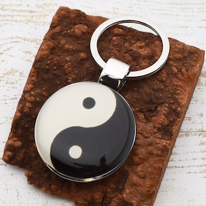 Könnte beinhalten: Ein silberner Schlüsselanhänger mit einem runden schwarzen und weißen Yin-Yang-Symbol-Anhänger.