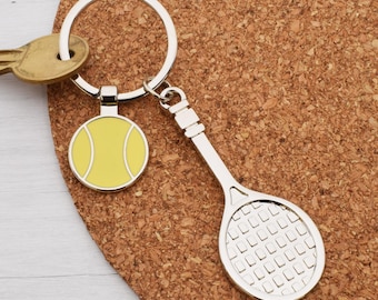 May include: A silver-colored tennis-themed keychain with a tennis ball charm and a tennis racket charm. The tennis ball charm is yellow with white accents. A gold-colored key is also visible.